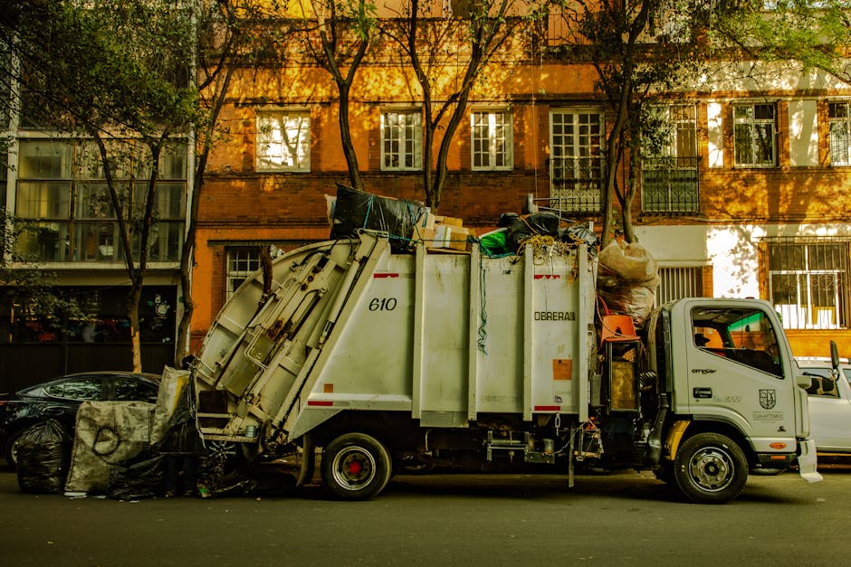 Three large black bin bags filled with rubbish are placed on a sidewalk near a curb, with the bags appearing to contain household waste or discarded items. The bags are made of durable plastic materia